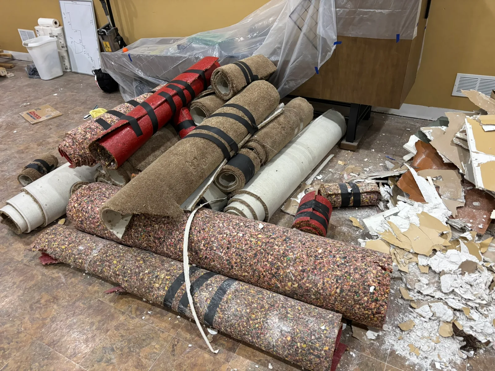 Rolled carpet, padding, and broken drywall piled beside covered furniture before removal